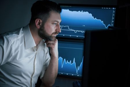 Full in the job. Bearded man in white shirt works in the office with multiple computer screens in index charts.